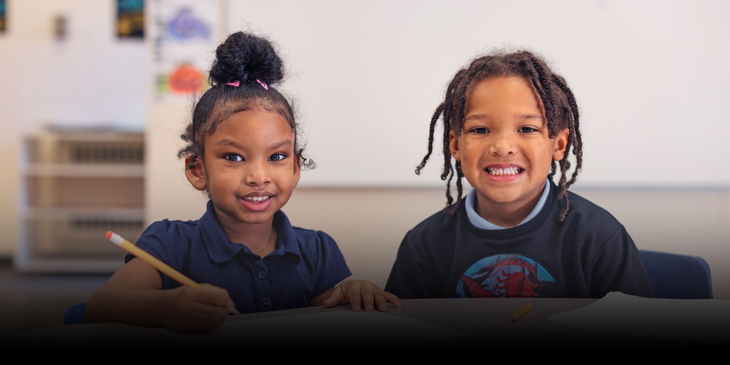 Smiling students in class with one holding pencil